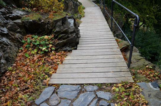 wooden bridge with forged metal railing. The bridge goes over a stone rock over an abyss in a gorge. the planks are thoughtfully dodging the stone that the carpenter had them toothed around. board
