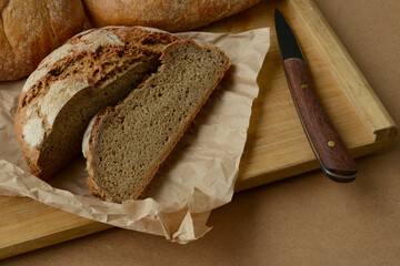 Fresh bread and a knife on a wooden background. Rye bread baked by hand at home or in a home bakery. Delicious natural black bread, cut into pieces with a knife