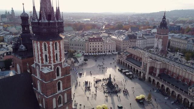 People Walking At Main Square With Adam Mickiewicz Monument, Cloth Hall And Town Hall Tower From St. Mary's Basilica In Krakow, Poland. - aerial pullback