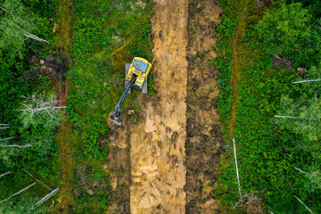 Naklejka premium Top down shot of excavator digging up material through forest for new subdivision.