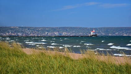 sea grass, waves,  sand, duluth,  and the wisconsin point lighthouse as seen from wisconsin point across lake superior on a sunny fall day in wisconsin