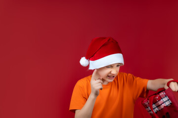 a boy in a Santa Claus Christmas hat holds a gift bag in front of him and shakes his finger