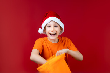 a boy in a Santa hat rummages in a yellow Christmas gift bag and laughs loudly