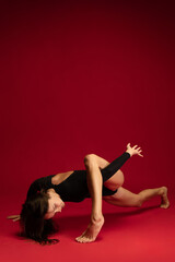 Obraz premium One emotional young flexible contemp dancer, ballerina jumping isolated on dark red background. Art, beauty, inspiration concept.
