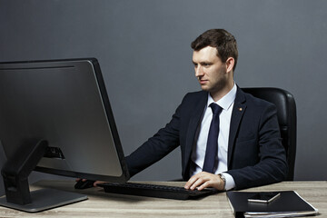 Young businessman working in office, sitting at desk, looking at laptop computer screen