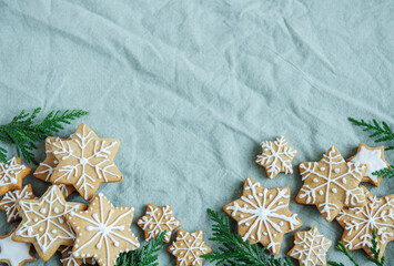 Spruce twigs with Christmas gingerbread cookies on the green linen crumpled textile background