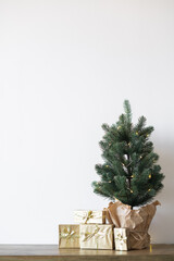 a small Christmas tree with warm bulbs in a pot on a wooden table with gifts wrapped in gold paper. the concept of Christmas