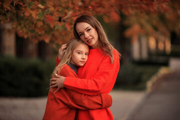 mother and daughter in orange sweaters have fun on a walk in the street near country houses