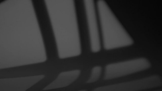 The shadow of a window moves along the surface of a gray wall at night in a room at home. Blurred background shadows with overlay effect, noise and grain texture.