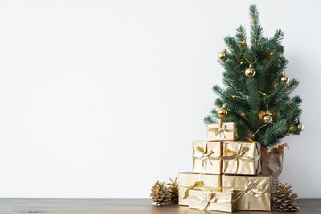 a small Christmas tree with warm bulbs in a pot on a wooden table with gifts wrapped in gold paper. the concept of Christmas