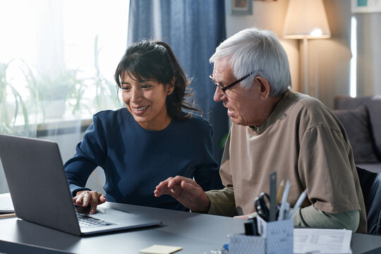 Friendly volunteer teaching to use the computer to senior man while they sitting at the table at home