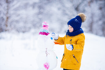 Little boy wearing bright clothes building a snowman on winter snowy day. Love winter and active...