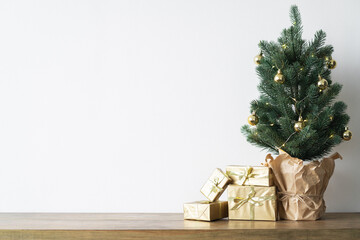a small Christmas tree with warm bulbs in a pot on a wooden table with gifts wrapped in gold paper. the concept of Christmas