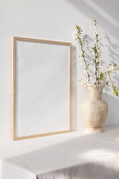 Wooden photo frame mockup with beige vase and flowering branches © PawStudioArt