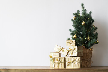 a small Christmas tree with warm bulbs in a pot on a wooden table with gifts wrapped in gold paper. the concept of Christmas