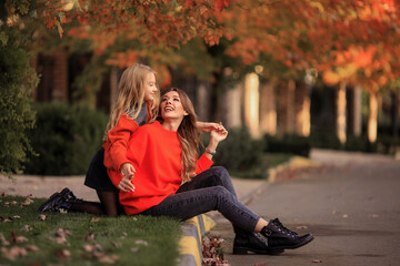 mother and daughter in orange sweaters have fun on a walk in the street near country houses