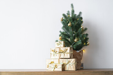 a small Christmas tree with warm bulbs in a pot on a wooden table with gifts wrapped in gold paper. the concept of Christmas