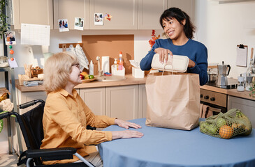 Smiling woman taking the food out of the paper bag at the table in the kitchen, she delivering food...