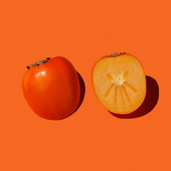 Cutaway persimmon on an orange background with hard shadows. Healthy food and nutrition concept.