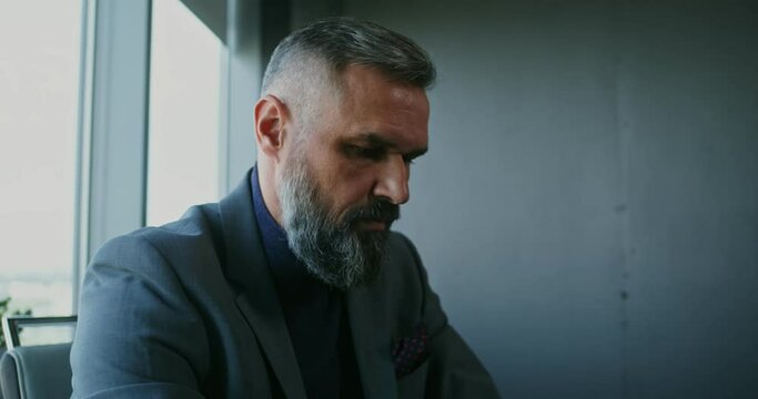 A respectable man uses a laptop sitting at a table in a modern office