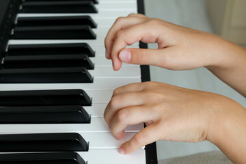 A little baby girl is playing a digital piano in the living room, hands close-up, A child learns to play a musical instrument. Early music education for children