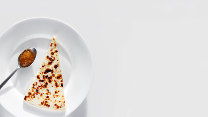 Slice of raditional finnish squeaky cheese served with cloudberry jam on the plate on white background.