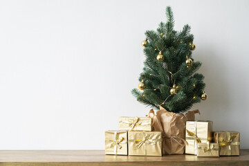 a small Christmas tree with warm bulbs in a pot on a wooden table with gifts wrapped in gold paper. the concept of Christmas