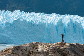 A woman stands on the rock formation and looks at the Perito Moreno Glacier