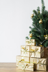 a small Christmas tree with warm bulbs in a pot on a wooden table with gifts wrapped in gold paper. the concept of Christmas