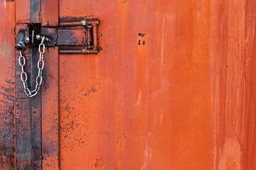 Old orange rusty iron door with lock, metal parts, bolt, nuts and shiny chain. Selective focus. Close-up