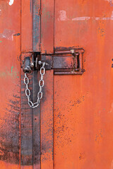 Old orange rusty iron door with lock, metal parts, bolt, nuts and shiny chain. Selective focus. Close-up