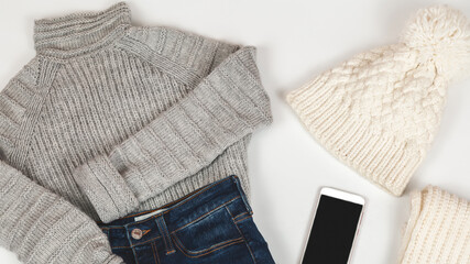 Winter hat with jeans, sweater, and scarf on white background. Women's stylish autumn or winter outfit. Trendy clothes collage. Flat lay, top view.