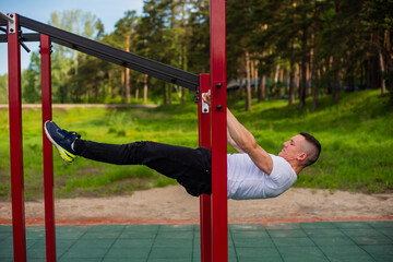 Caucasian man doing a back plank on the uneven bars. Workout on the sports ground.