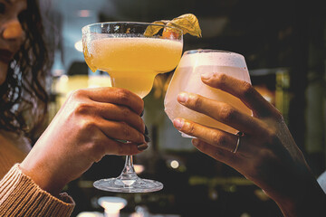 Girlfriends toasting with cocktail glasses indoor - closeup on hands - unrecognizable persons
