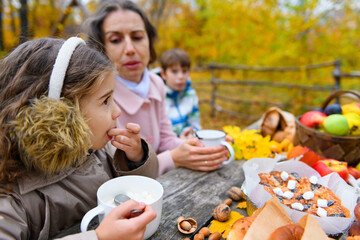 Portrait of a happy family in an autumn park. People are sitting at the table, eating and talking. Posing against the background of beautiful yellow trees. They are happy together.