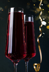 Festive background. Pink drink in glass champagne glasses with bokeh and tinsel on a black background