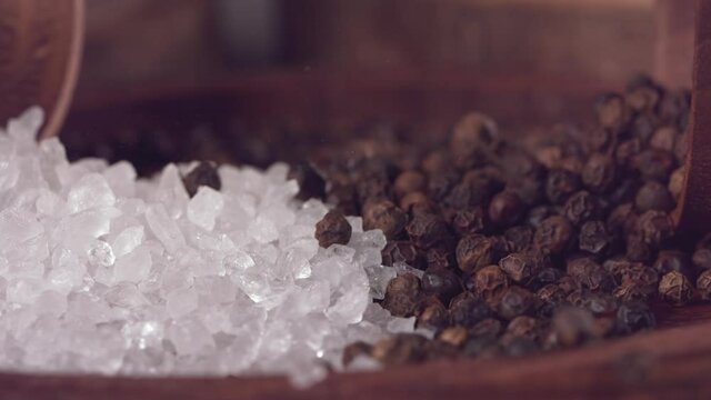 Black pepper and salt colliding on a wooden table. Slow motion. Close up