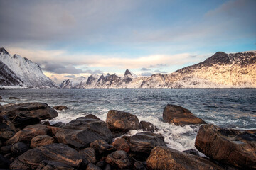 Snow mountain range and wave hitting on coastline in winter at Senja island