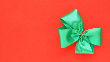 Top view, green tied bow on red background. Space for your text, concept for Christmas decoration..