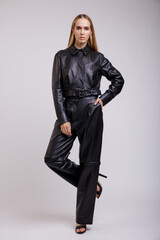 High fashion photo of a beautiful elegant young woman in a pretty leather suit, pants, jacket posing on white background. Studio Shot. Slim figure