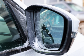 Side mirror of a white new snow-covered car with a reflection covered with frost on a sunny bright frosty day in the Urals. Selective focus. Close-up