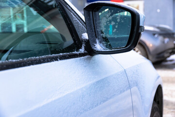 Obraz premium Side mirror of a white new snow-covered car with a reflection covered with frost on a sunny bright frosty day in the Urals. Selective focus. Close-up