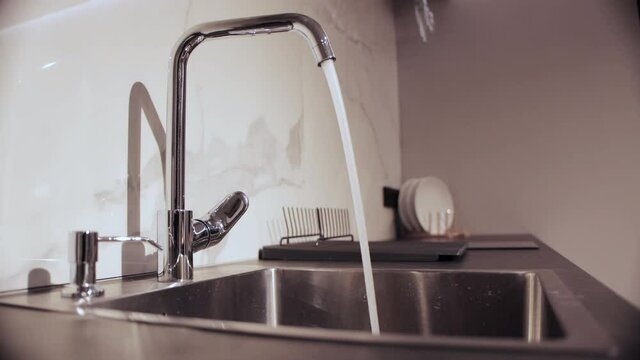 The man opens and closes the water faucet in the kitchen. Concept of utility bills for water supply. Copy space for text