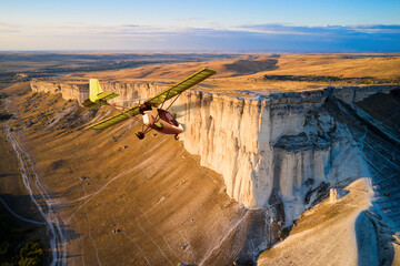 A sports plane flies around a white rock. Shooting from the air. Copy space.