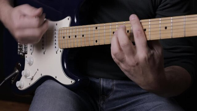 A male musician plays a melody on a blue six-string guitar.