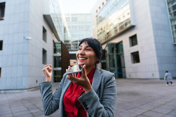 Latina business woman sending voice messages on her mobile phone on the street.