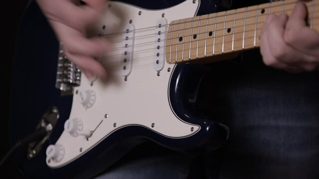 A male musician plays a melody on a blue six-string guitar.