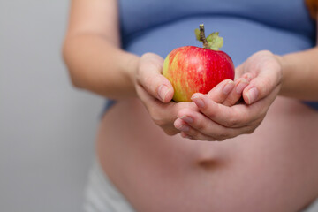 Pregnant woman holding apple on grey studio backgroun , pregnancy and healthy eating concept