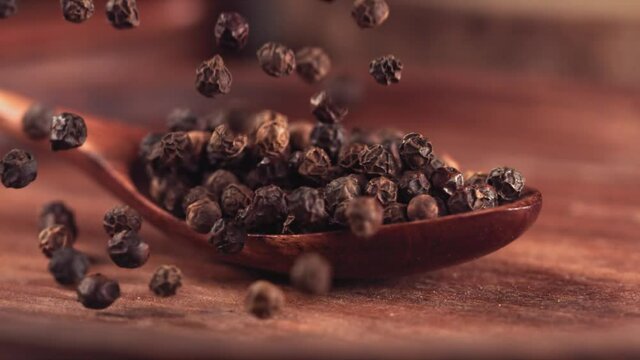 Black pepper falling on a wooden spoon.Slow motion. Close up
