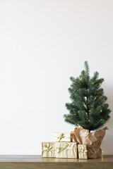 a small Christmas tree with warm bulbs in a pot on a wooden table with gifts wrapped in gold paper. the concept of Christmas